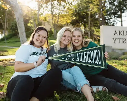 Three female Concordia students holding a school flag